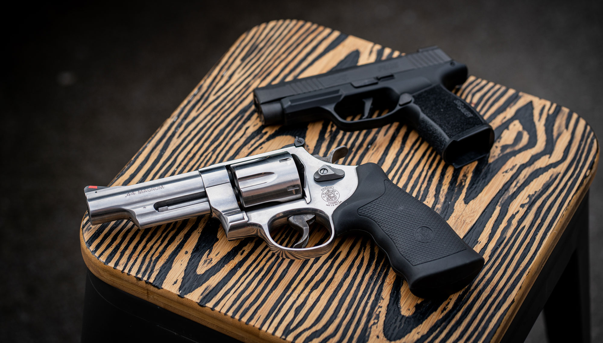 A Smith & Wesson 44 magnum revolver next to a Sig Sauer pistol on a bench.